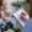 Woman blurry in background talking, woman holding a clip board and writing something in the foreground, in focus. The camera angle is over the shoulder of the woman holding the clip board.